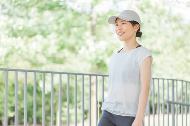 晴れた公園を笑顔でウォーキングしている女性の写真